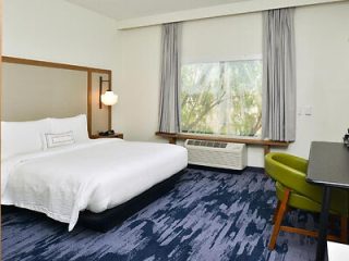 Modern hotel room with a king-sized bed, large window overlooking greenery, and a green chair at a work desk.